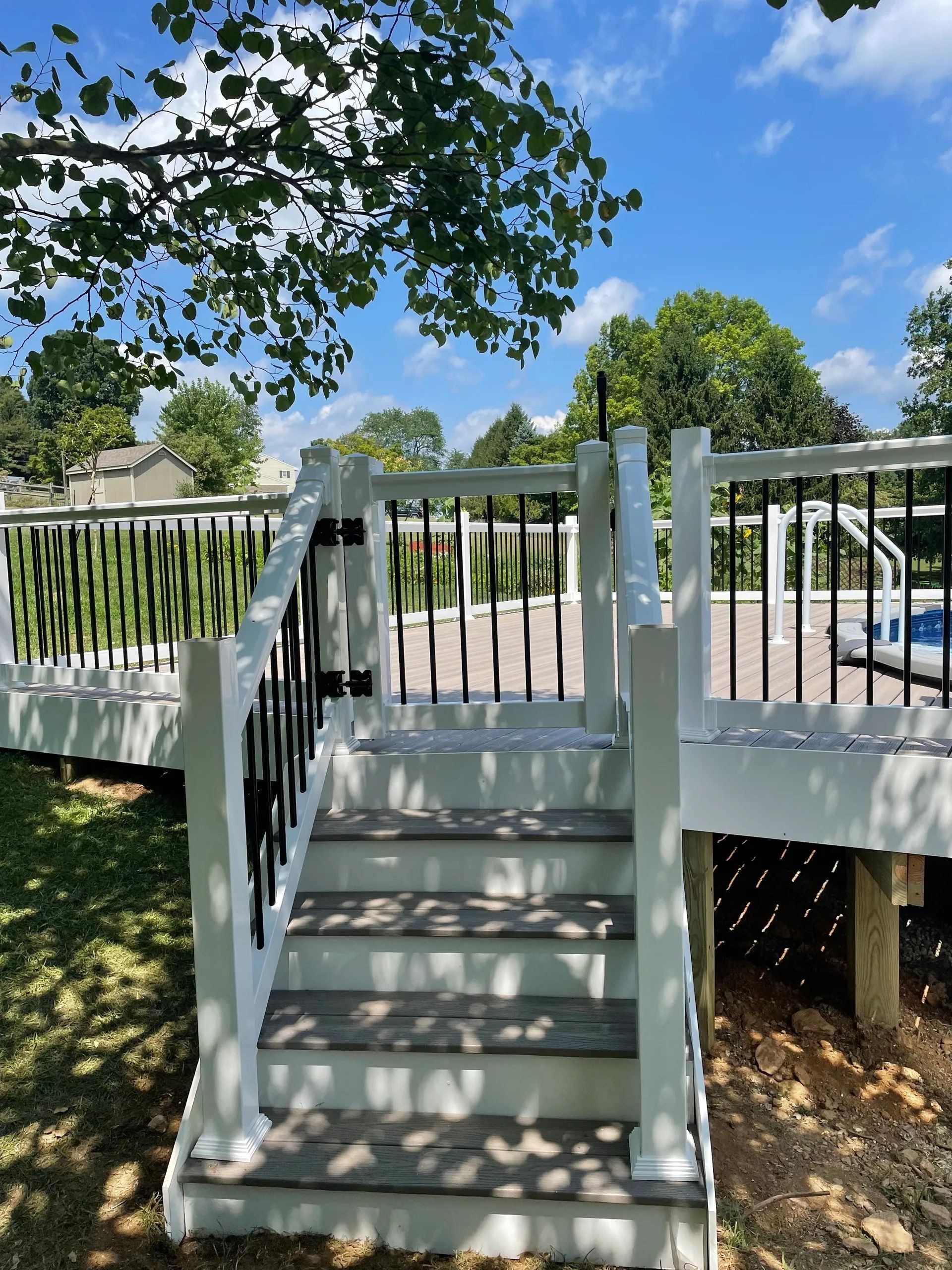 Stairs leading up to a white deck with black railings, a pool in the background under a sunny sky.