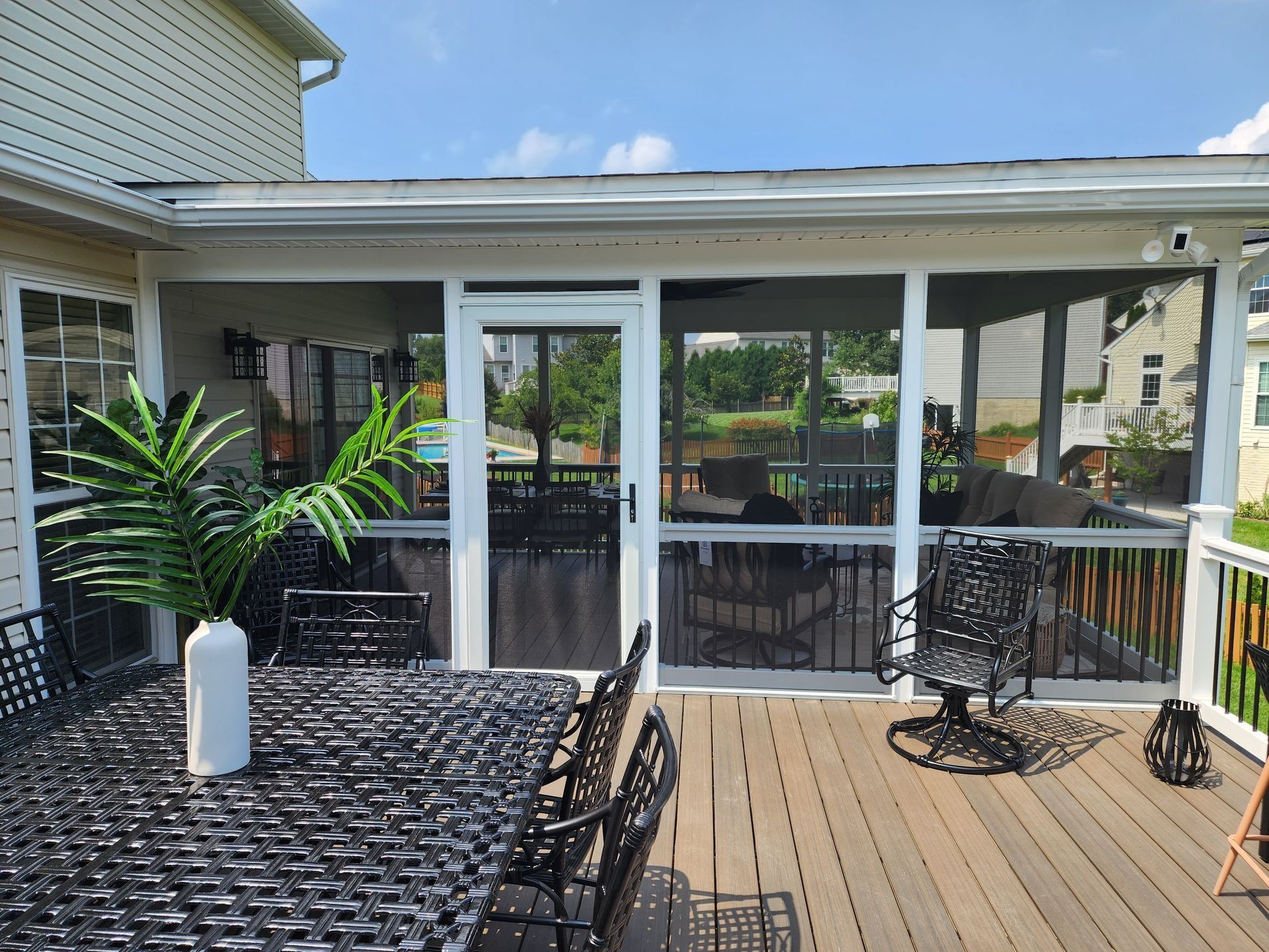 Outdoor screened porch with patio furniture. Brown deck, black furniture, white trim, and green foliage.