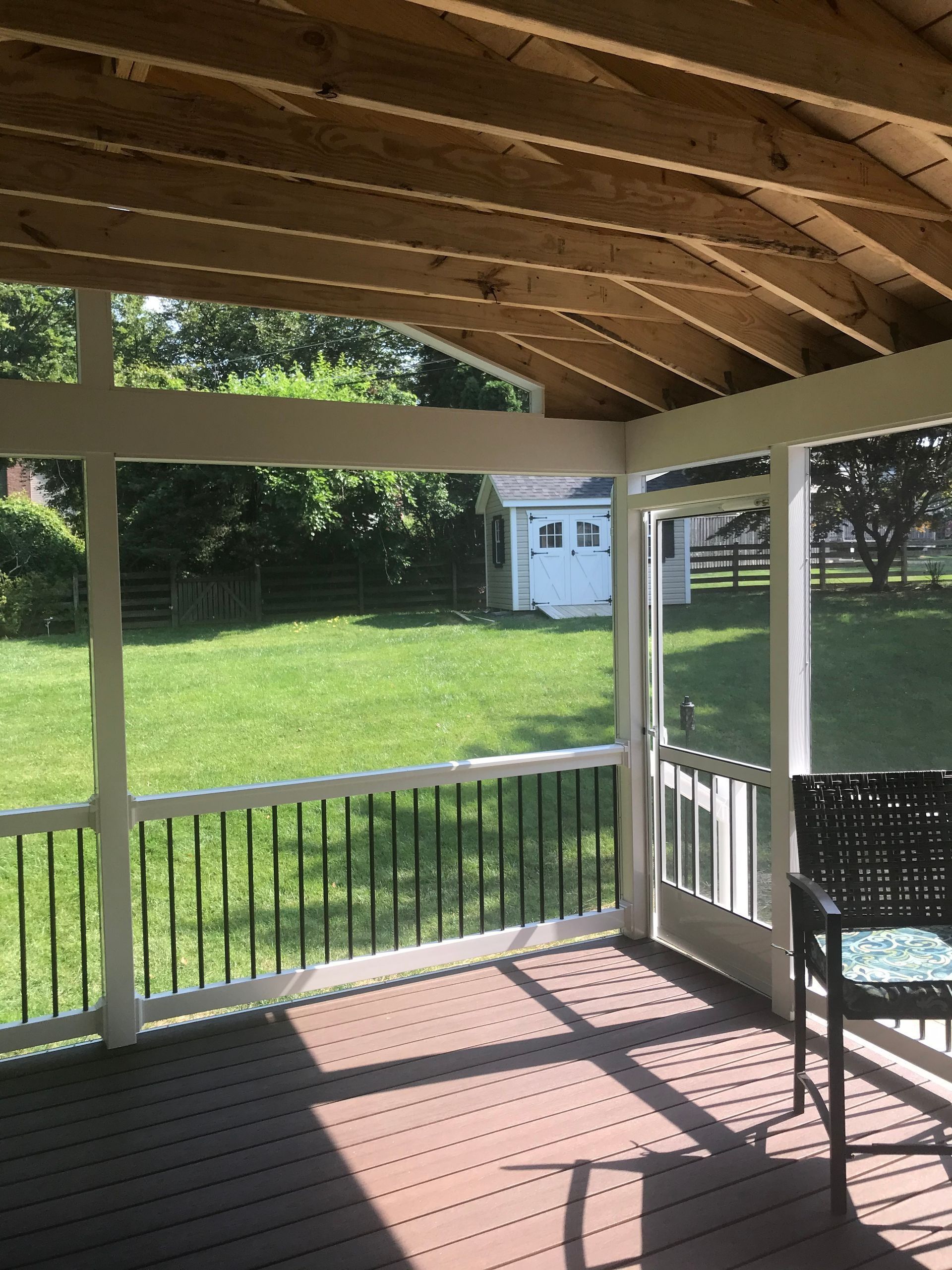 Screened porch with dark flooring, white trim, black railing, and view of green yard and shed.