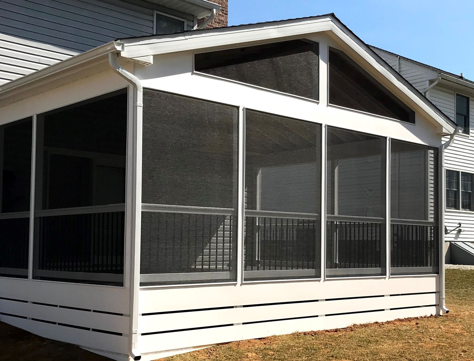 Screened-in porch with white siding, black screens, and a black railing, attached to a house with white siding.