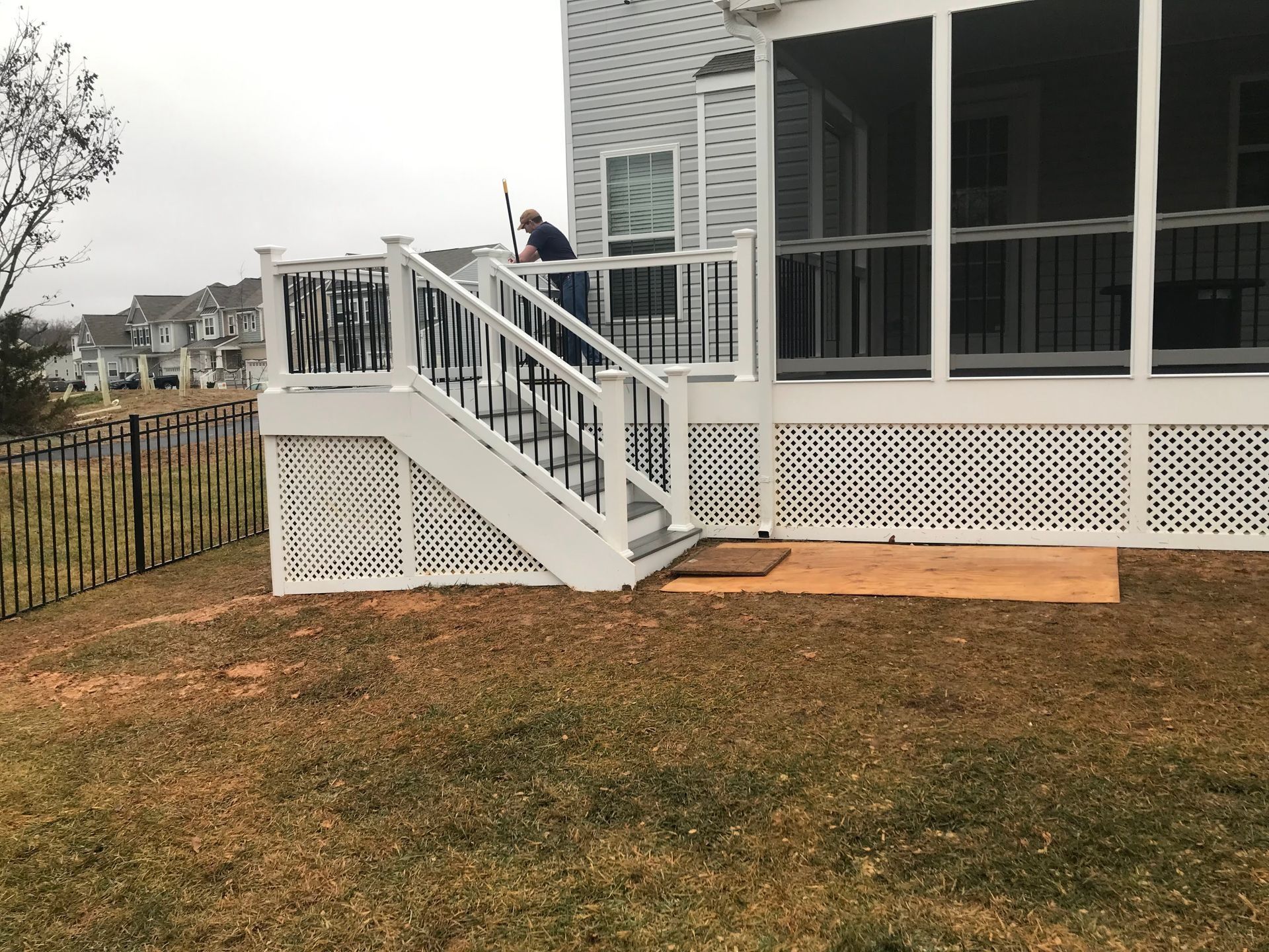 White deck with stairs, person on deck, brown grass, houses in background.