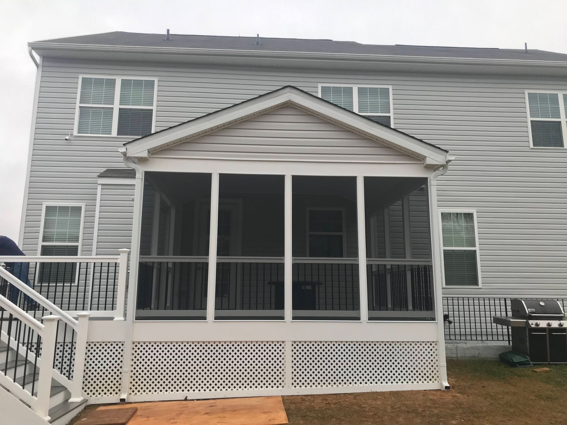 A screened porch attached to a two-story gray house with a white deck and railing.