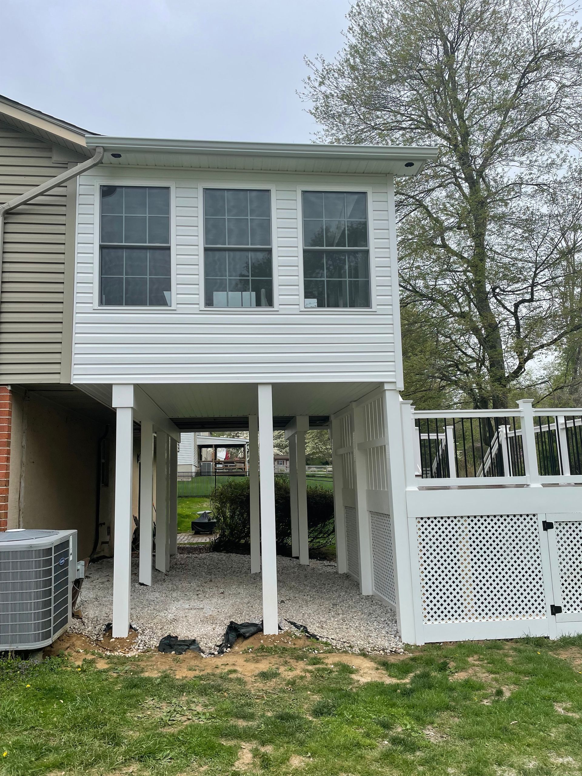 White two-story deck addition to a house, supported by white columns, with a gravel ground.