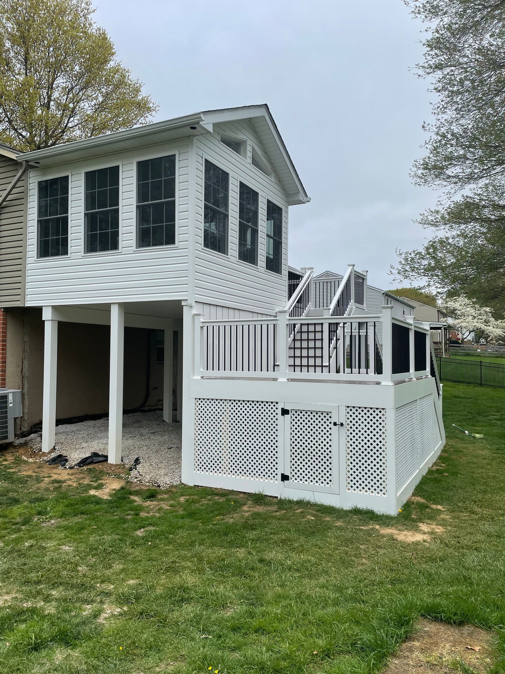 White two-story house with deck, black shutters, on green lawn, against a cloudy sky.