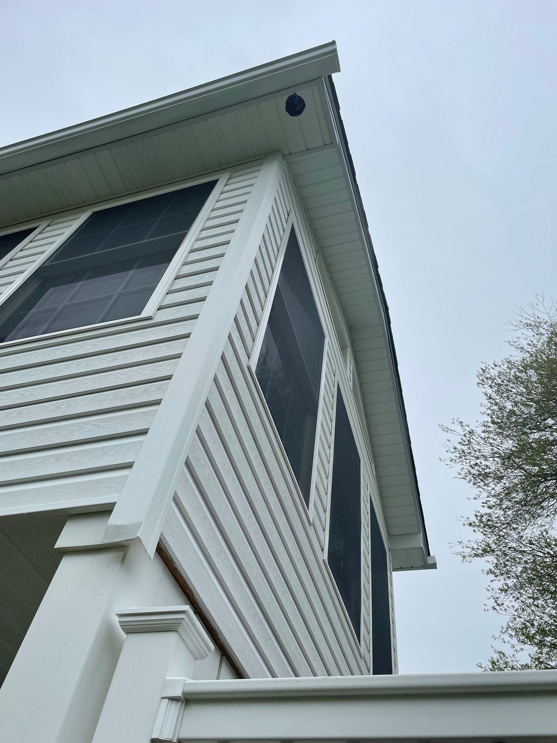 White screened porch with vinyl siding against a cloudy sky.