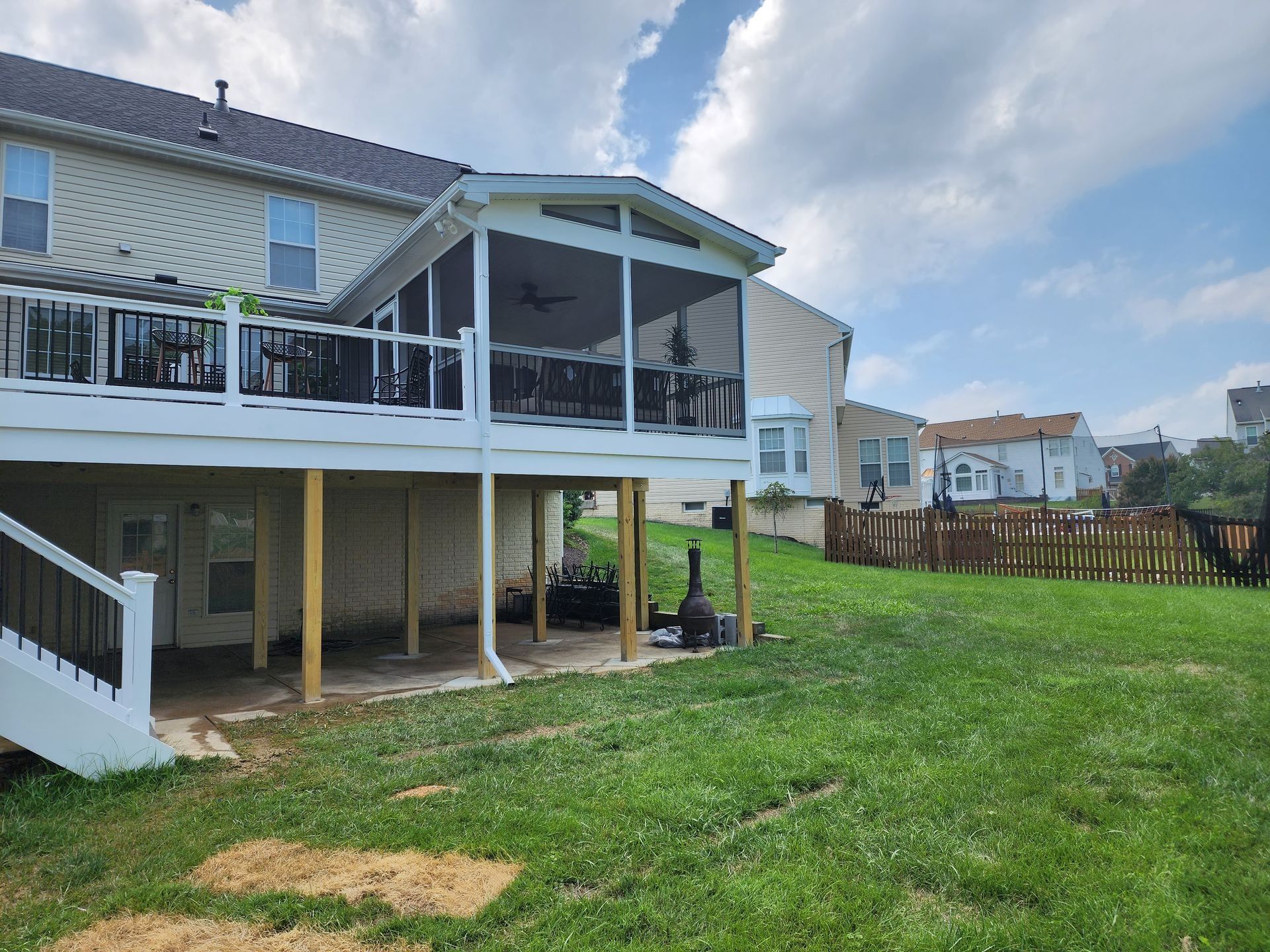 Backyard with a screened porch attached to a two-story house, wooden fence, and green lawn.