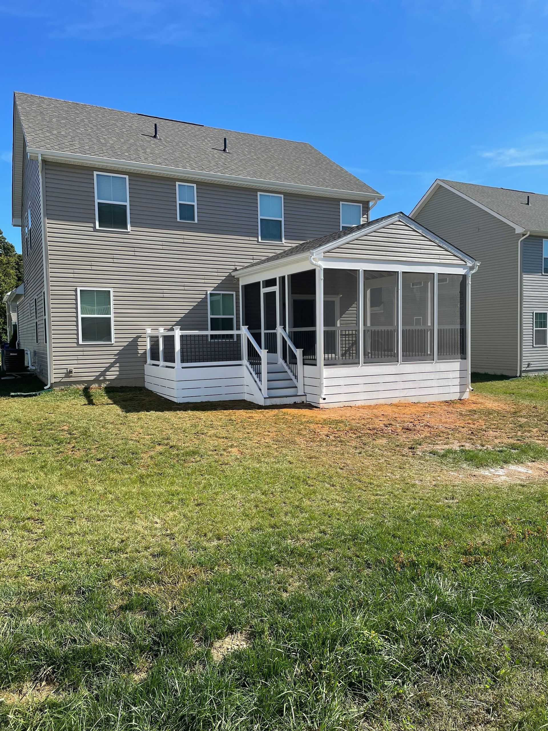 Two-story house with attached white screened-in porch and deck, set on a grassy lawn under a blue sky.