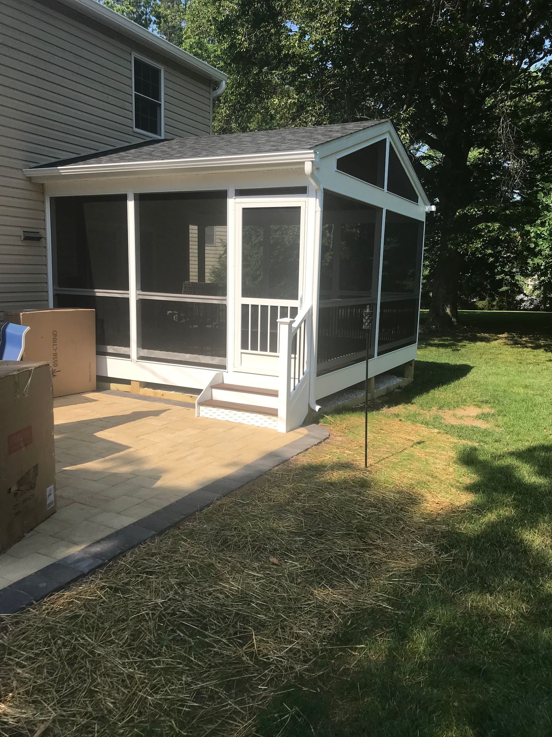 Screened porch with white trim attached to a beige house, on a concrete patio, green grass.