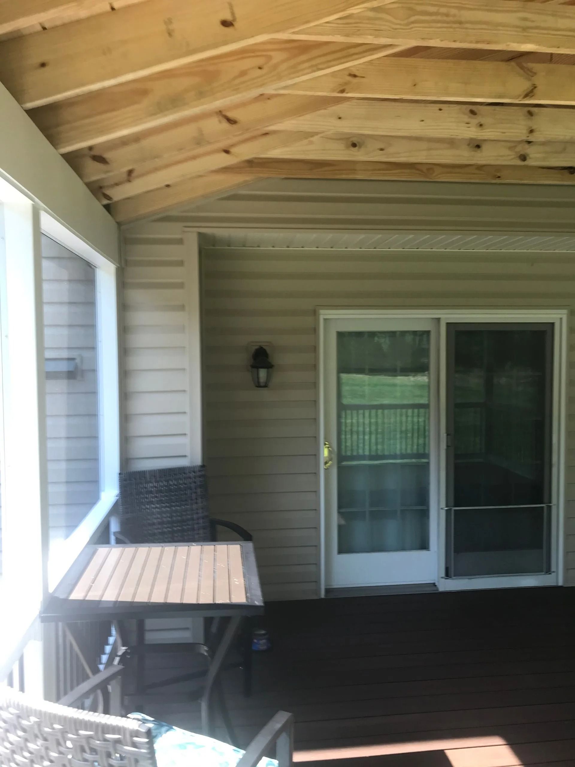 Screened-in porch with a table and chairs, sliding glass door, and light-colored siding under a wooden ceiling.
