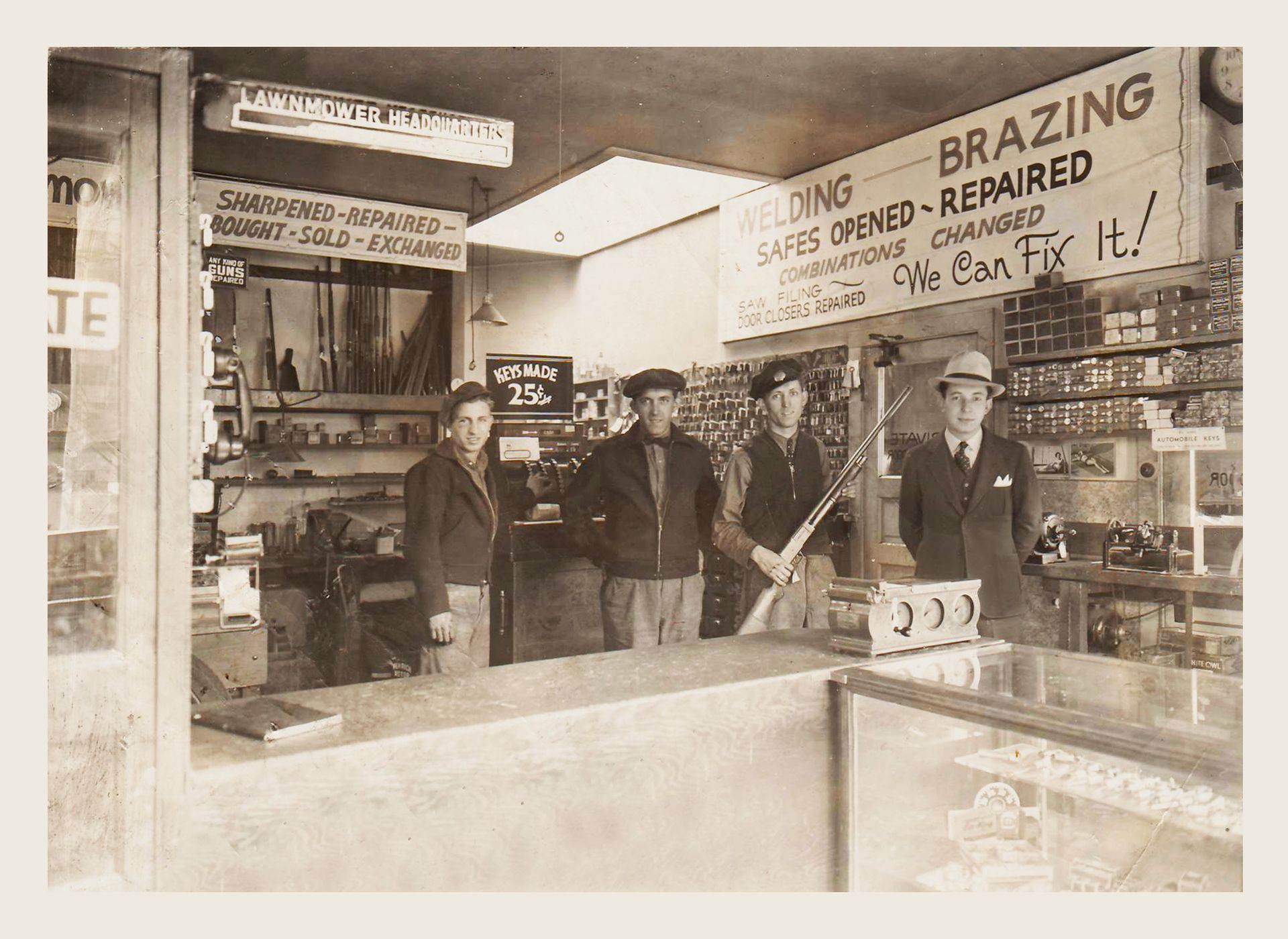 Four men standing behind a shop counter; a sign advertises welding, brazing, and repairs.