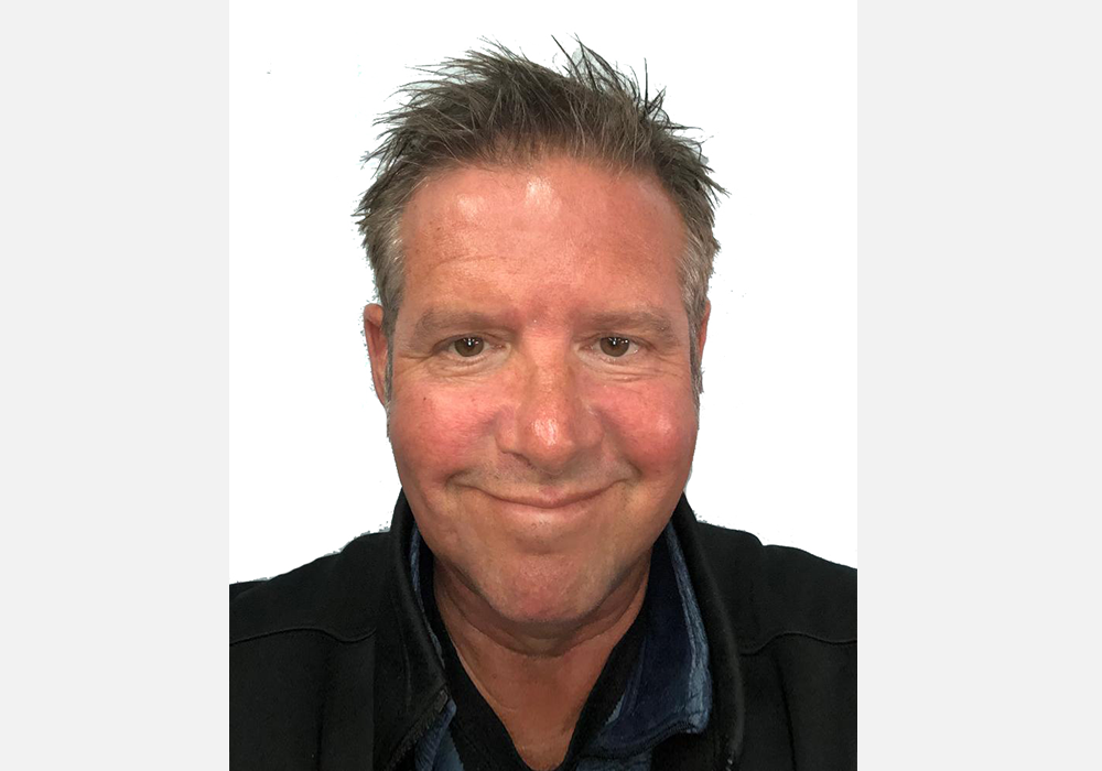 Smiling man with short spiky hair, wearing a black jacket, against a white background