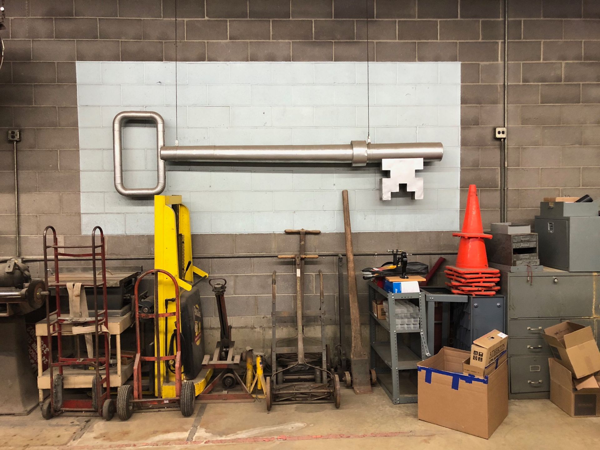 Large metal key sculpture mounted on a light blue painted wall, surrounded by tools and equipment in a workshop setting.