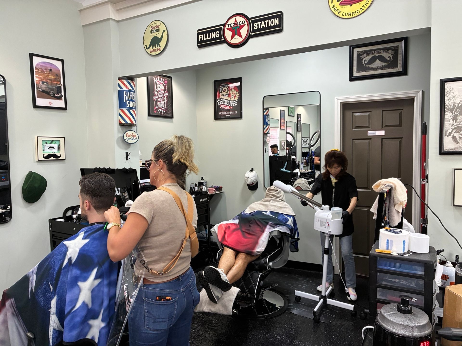 Hair salon with a client in a blue cape and a stylist working on hair beside a mirrored station.