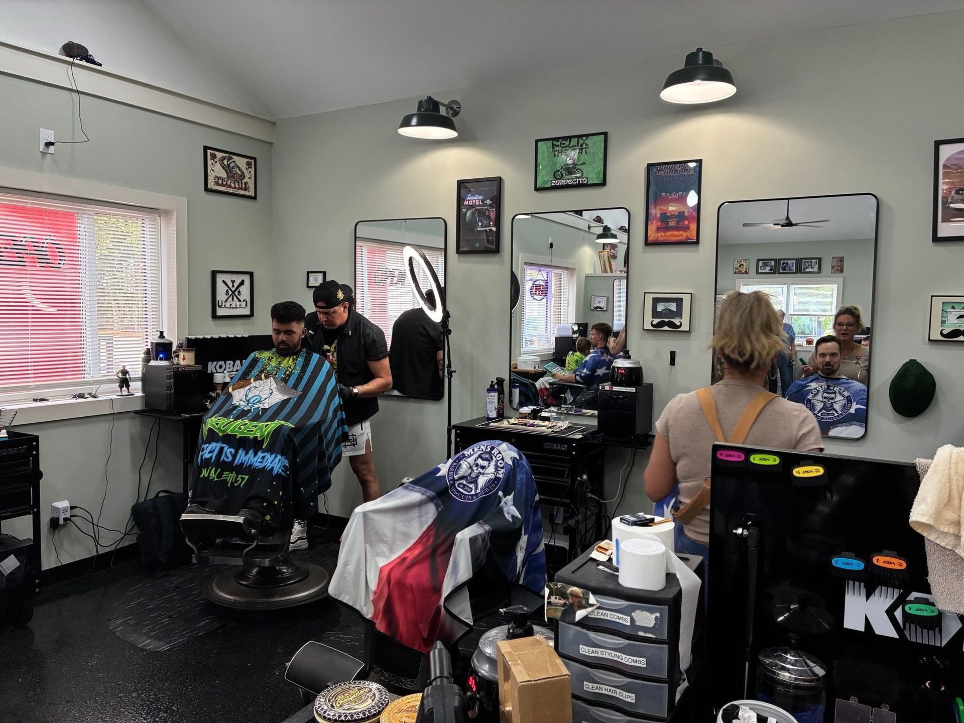 Busy barbershop interior with two clients getting haircuts and stylists working at stations