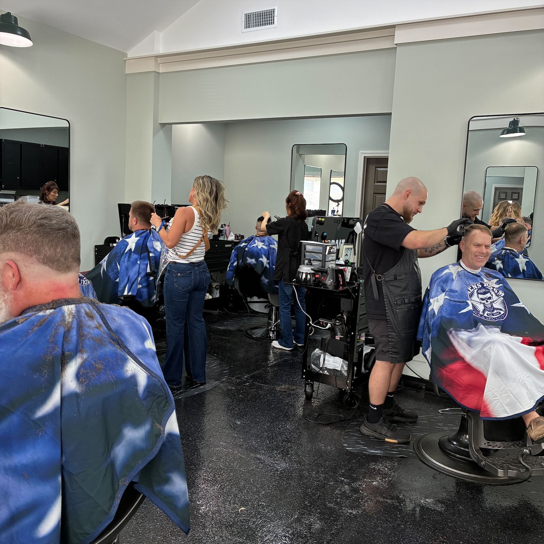 Hair salon with clients in capes getting haircuts and stylists working around mirrors.