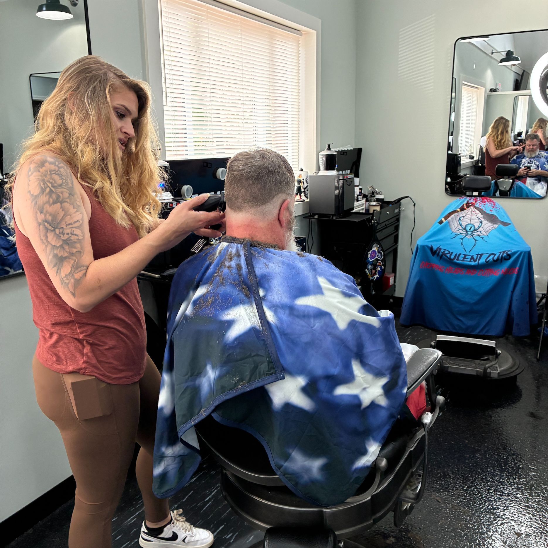 Stylist cutting a client’s hair in a salon chair, with a blue cape and mirror reflection nearby