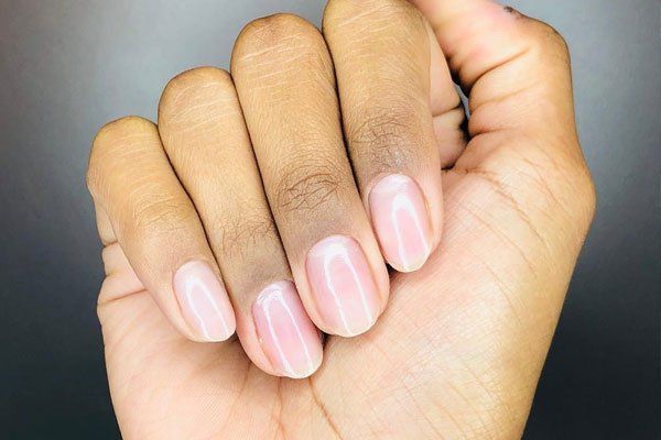 Hand with oval-shaped, light pink polished fingernails against a dark background