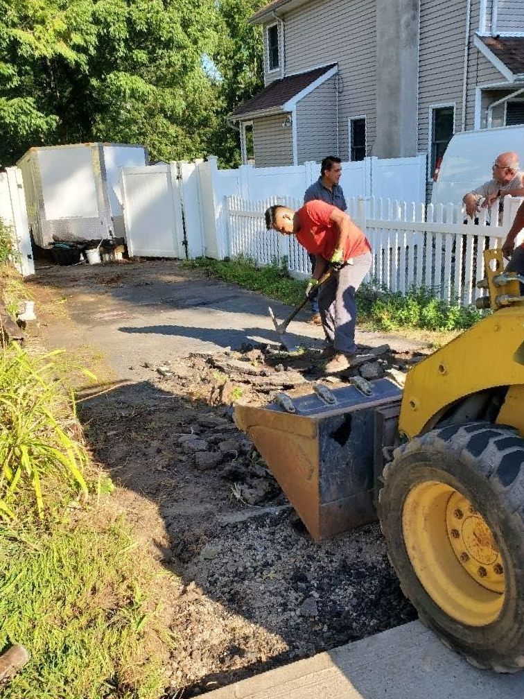 A man is digging in the dirt next to a yellow tractor.