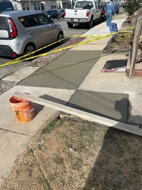 A bucket of concrete is sitting on the side of a sidewalk.