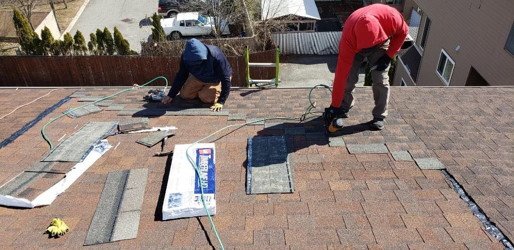 Two men are working on a roof and one of them is wearing a red jacket