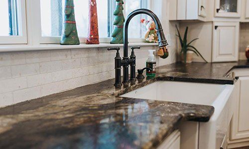 A kitchen sink with a black faucet and granite counter tops.