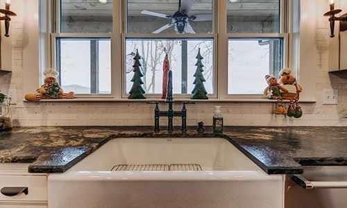 A kitchen sink with a christmas tree on the window sill.
