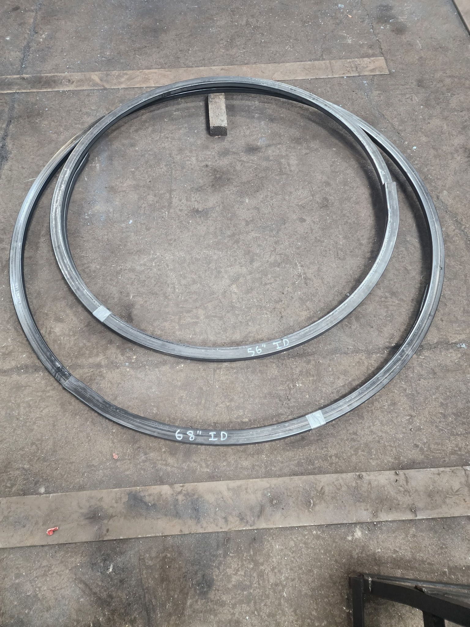 Two black, circular, toothed metal gear rings of different sizes lying on a concrete surface.