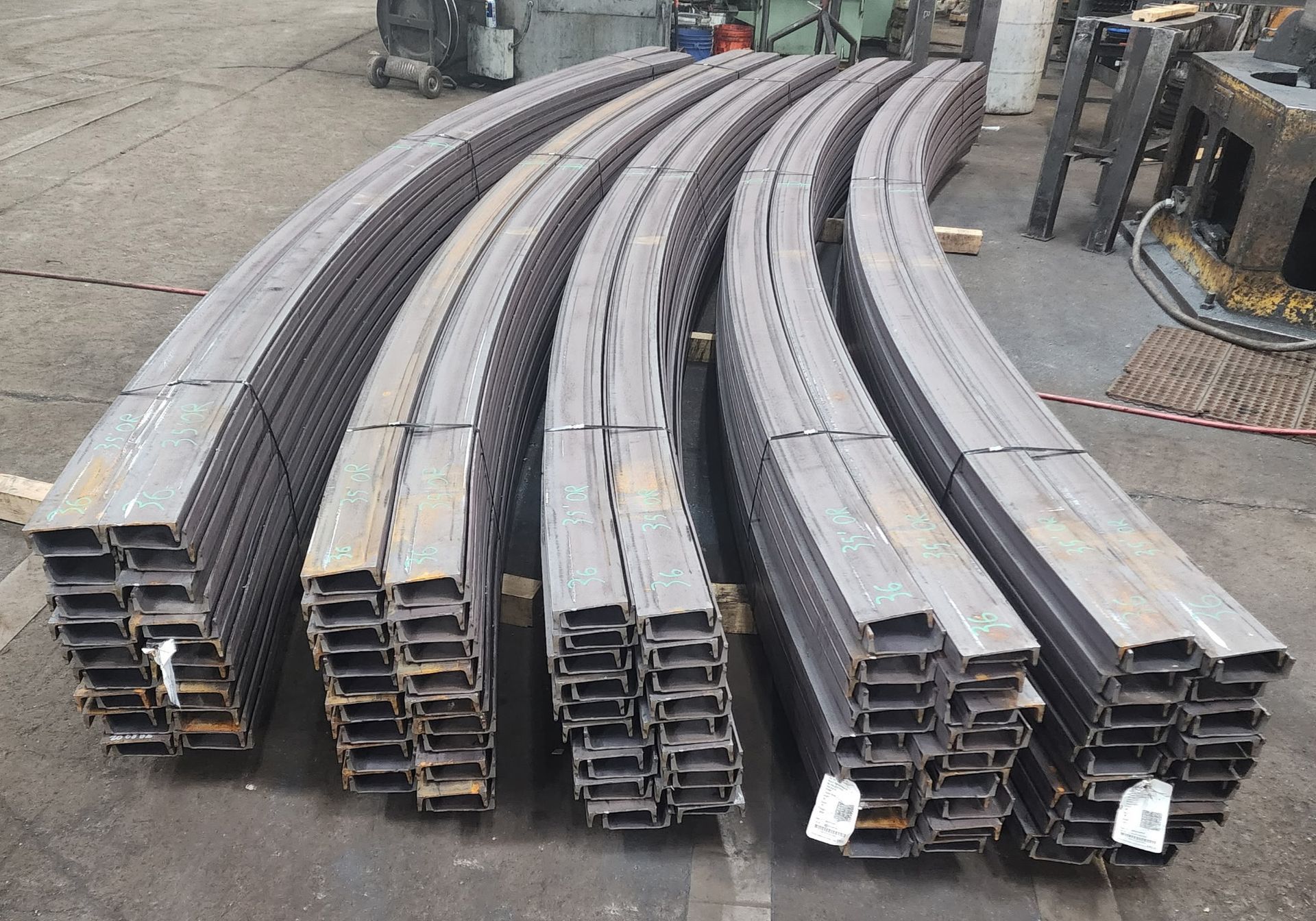 Several stacks of curved steel channels arranged in rows on a concrete factory floor.