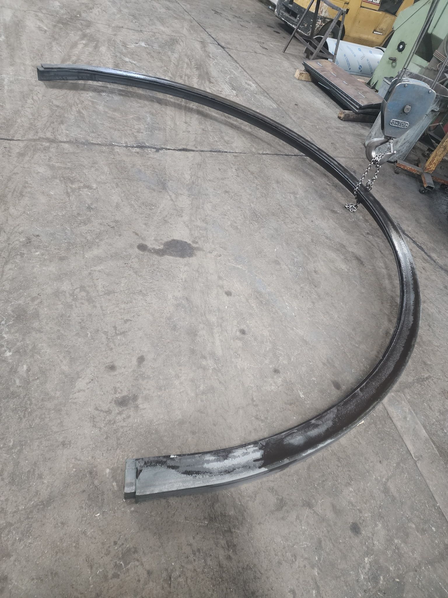 Curved metal bar on a concrete surface, likely industrial setting.