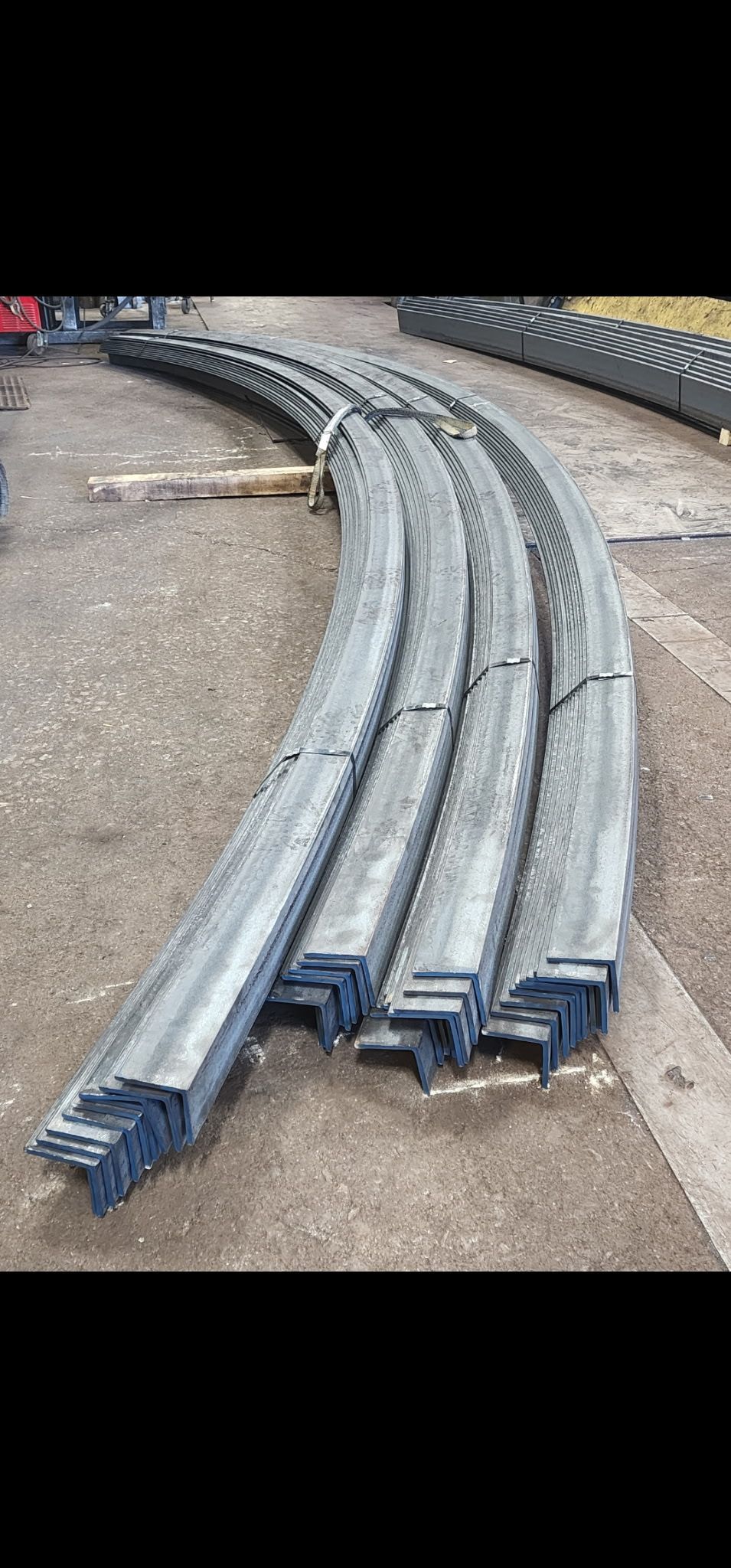 Curved metal beams stacked on gravel ground.