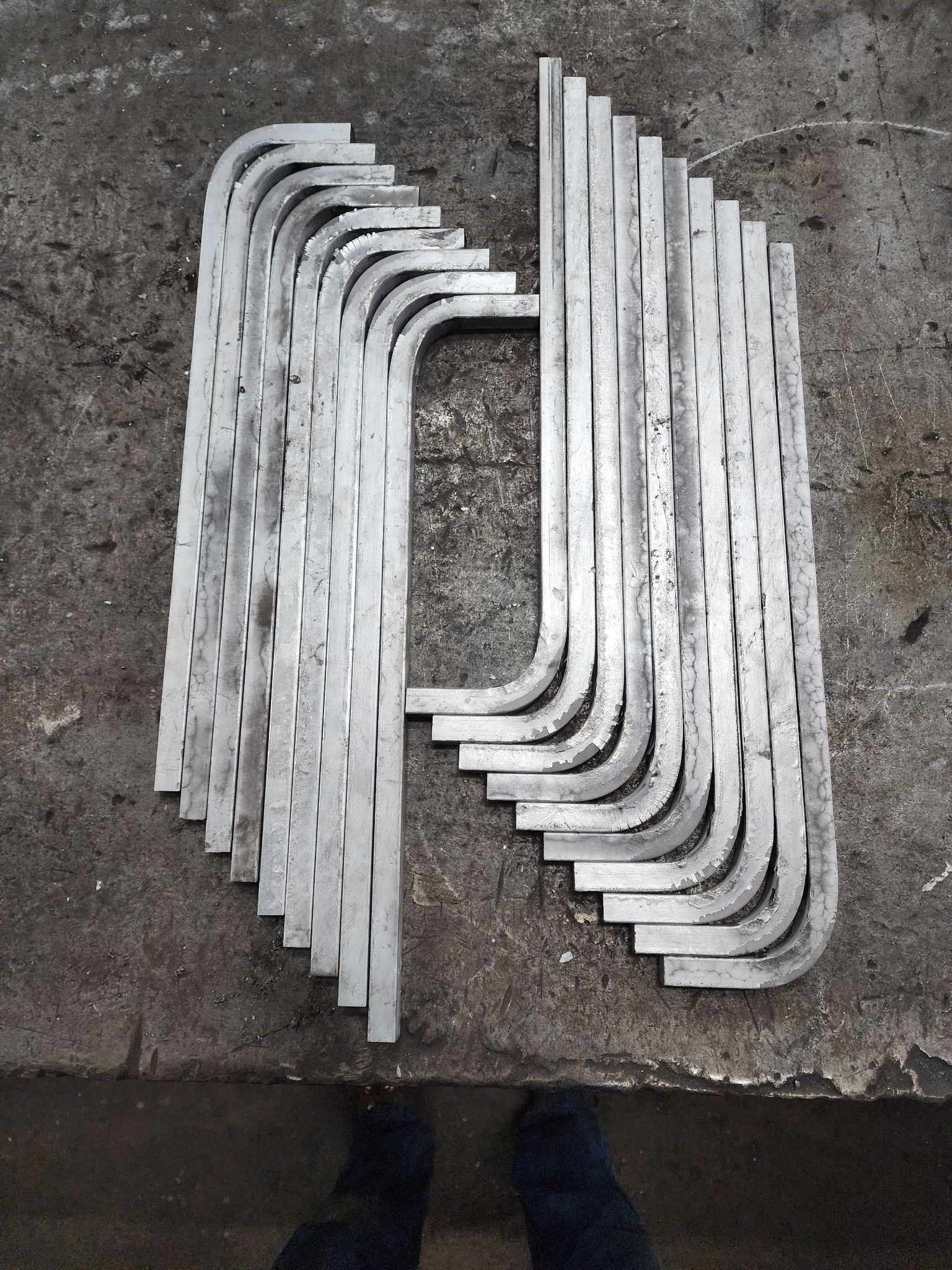 Metal brackets, silver color, stacked on a gray concrete surface.