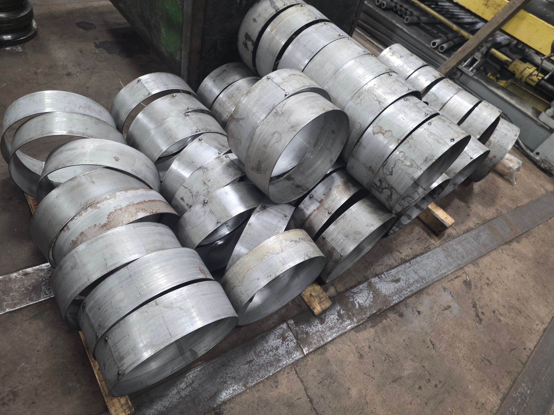 Stacks of cylindrical metal rings on a wooden pallet in a workshop setting.