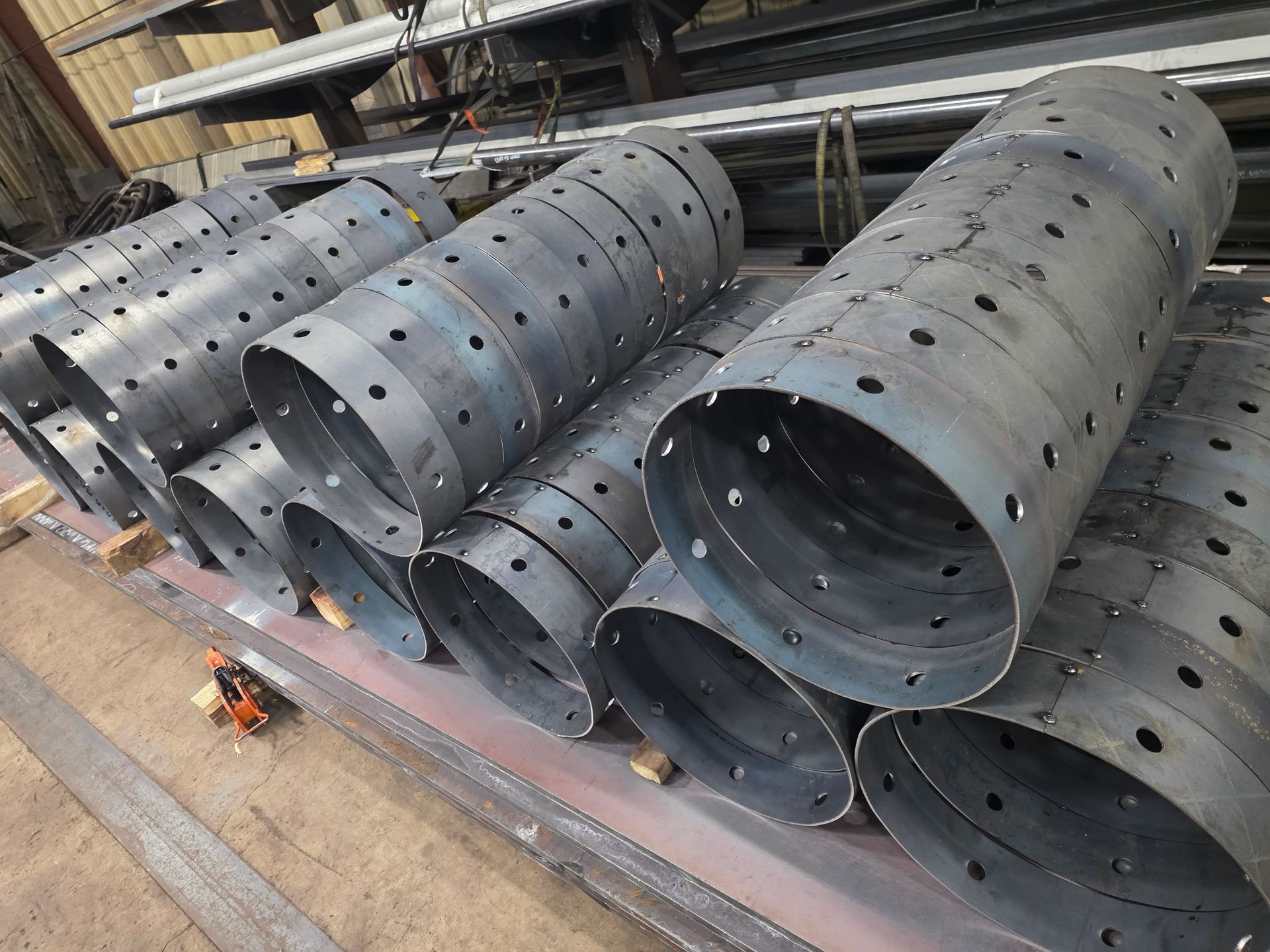Metal cylinders with evenly spaced holes, stacked on a metal surface, in a workshop setting.