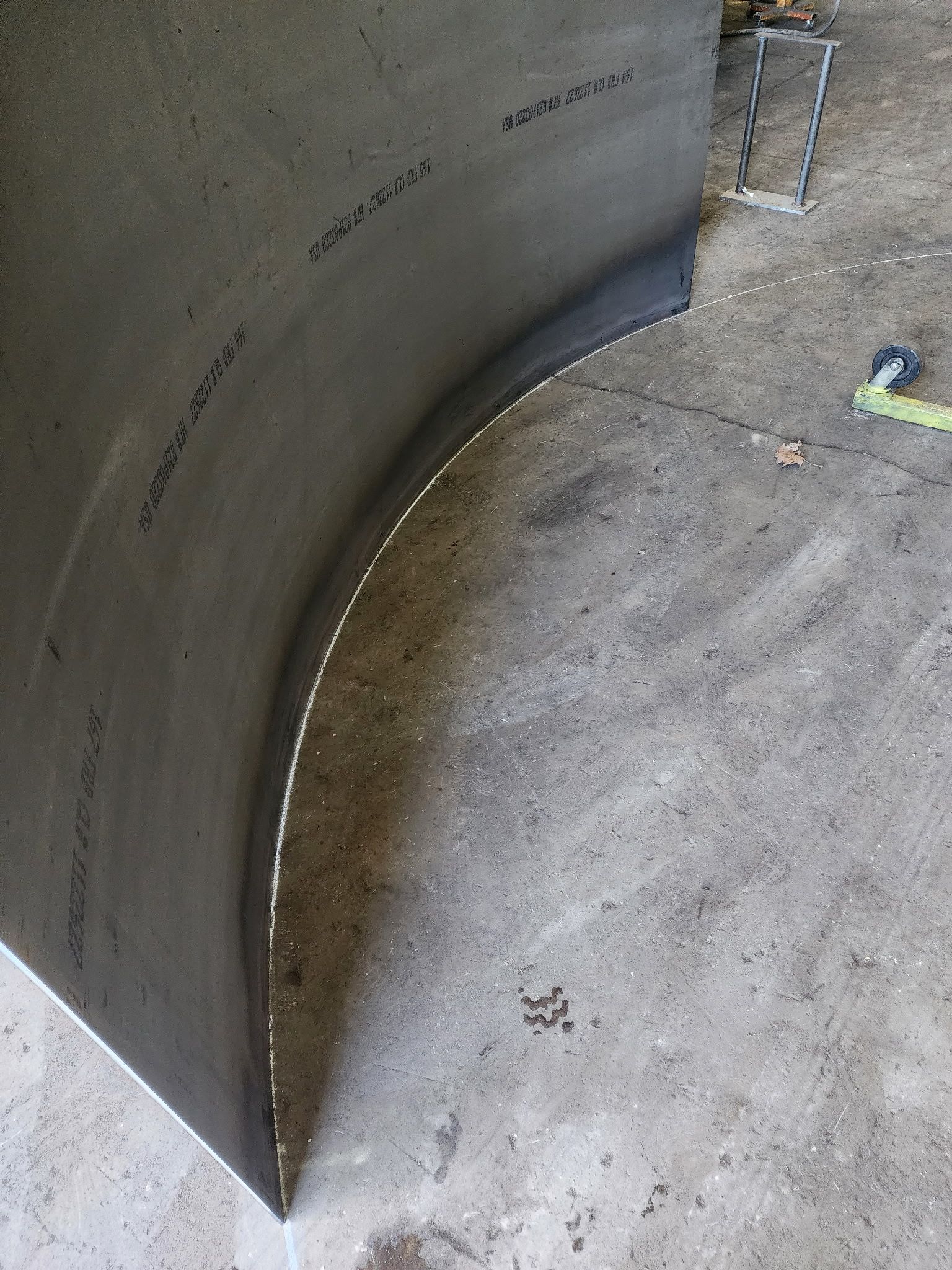 Curved dark panel, marked with text, edge trimmed with white. Gray concrete floor.