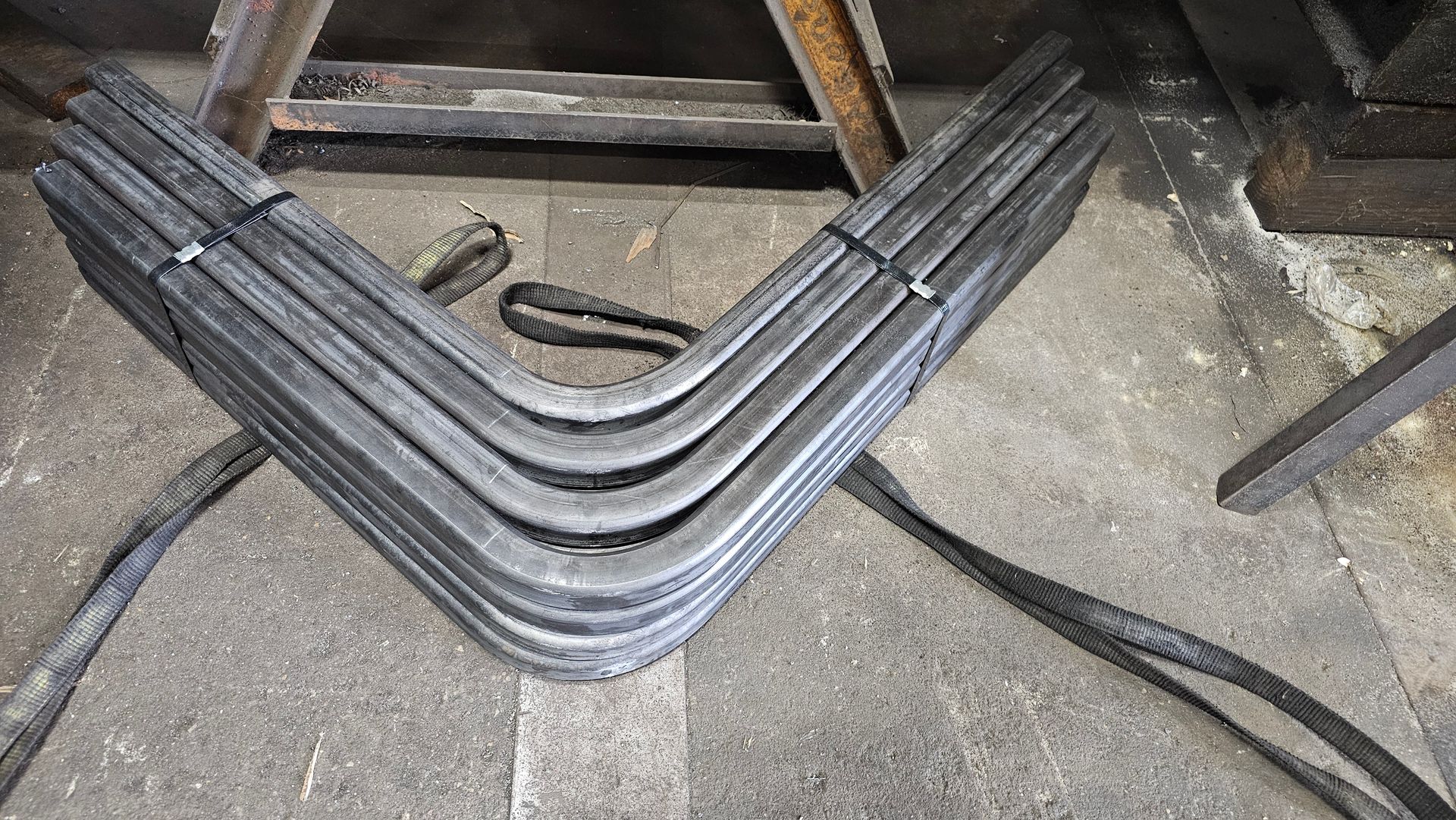 Bundle of bent metal pieces, V-shaped with rounded corners, on a concrete surface.