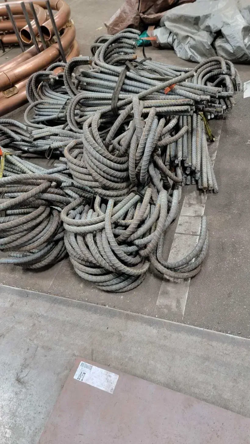 Bundles of steel rebar loops on a concrete floor in a workshop, copper pipes in the background.