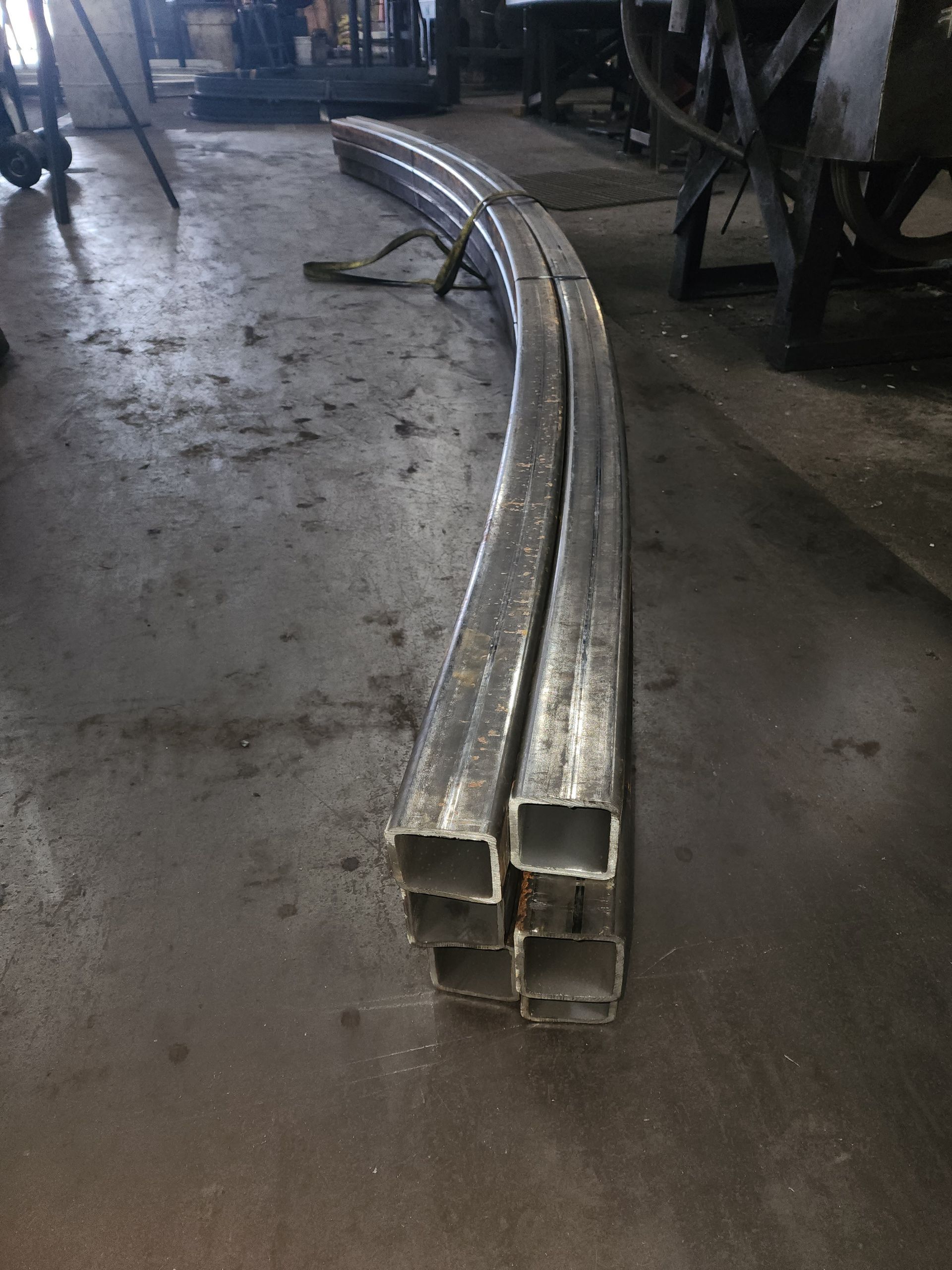 Four curved, square metal tubes stacked on a dirty floor.