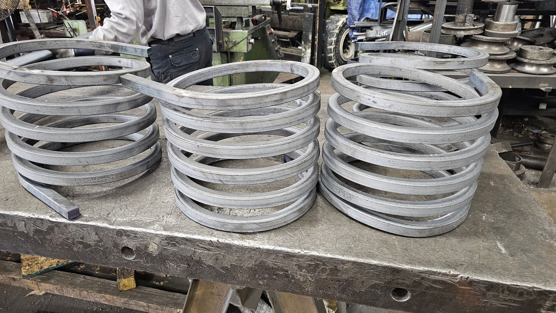 Three metal coils on a workbench with a person in the background, workshop setting.