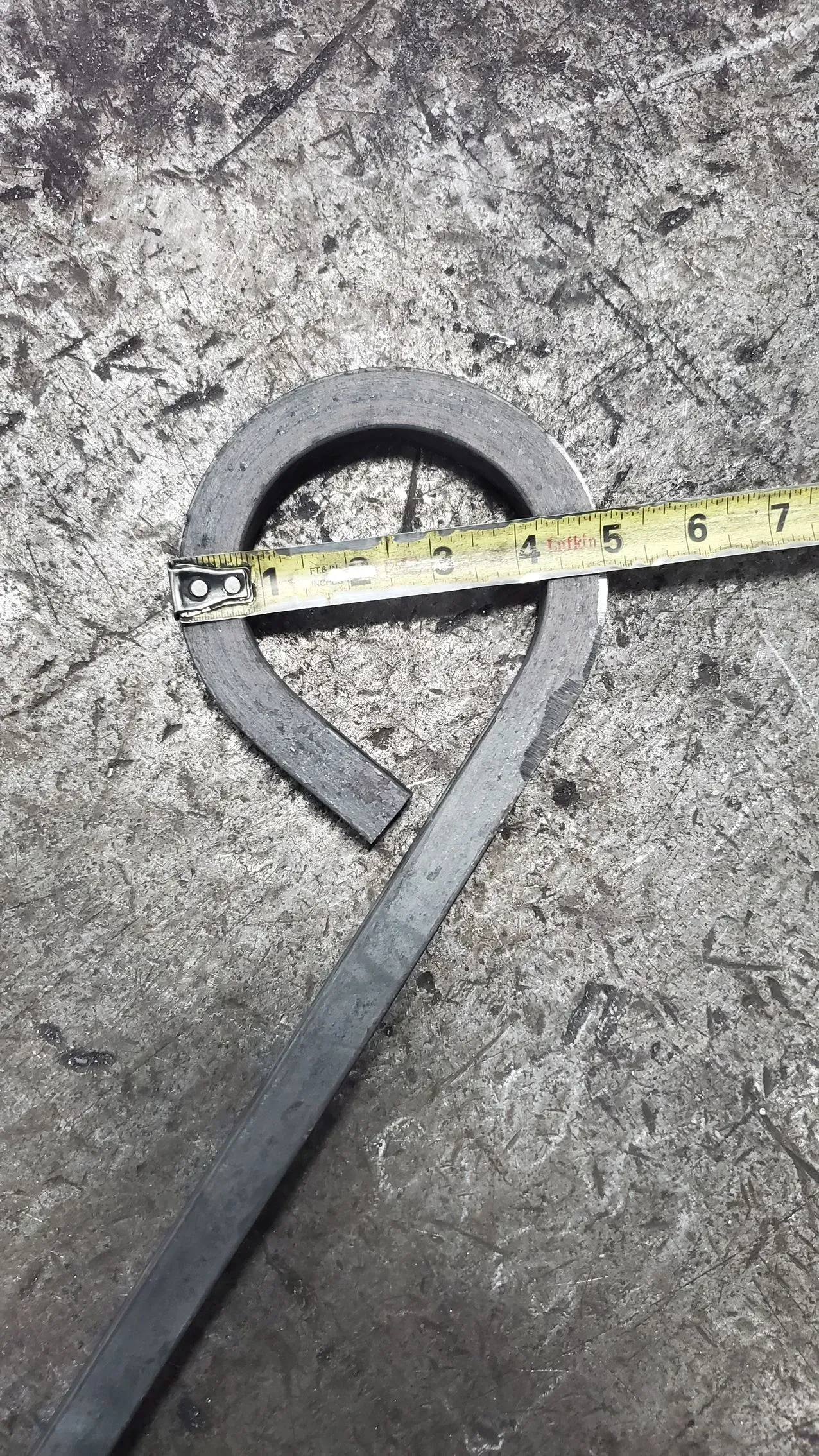 Metal ring with attached handle, measured with a tape measure.