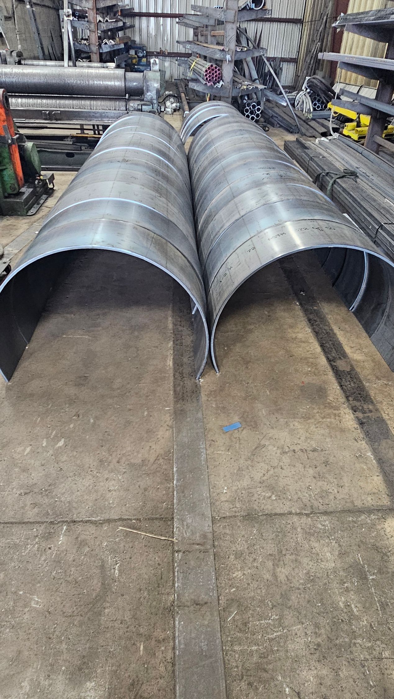 Two curved metal sheets lie on a concrete floor in a workshop.