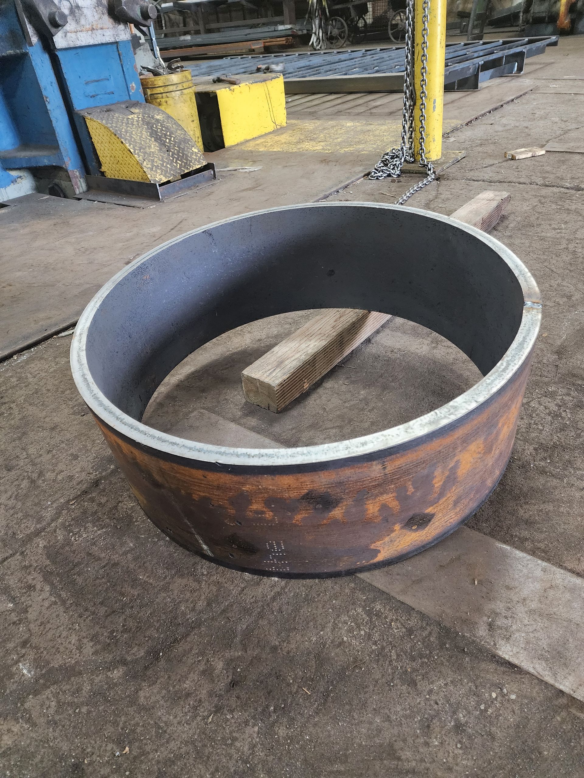 Cylindrical steel ring, rusty exterior, gray interior, lying on concrete floor, wood block inside.