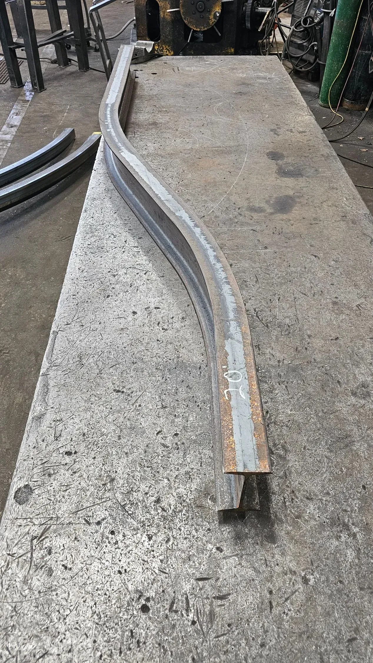 Curved metal beam on a rough stone surface, possibly in a workshop.