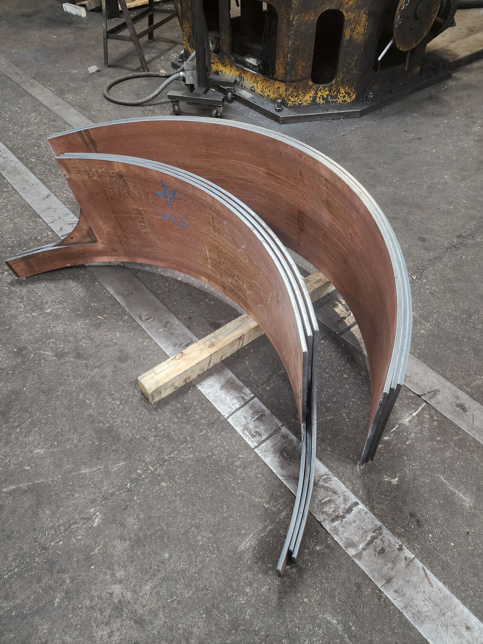 Two curved, rusty metal pieces on a wooden support in an industrial setting.