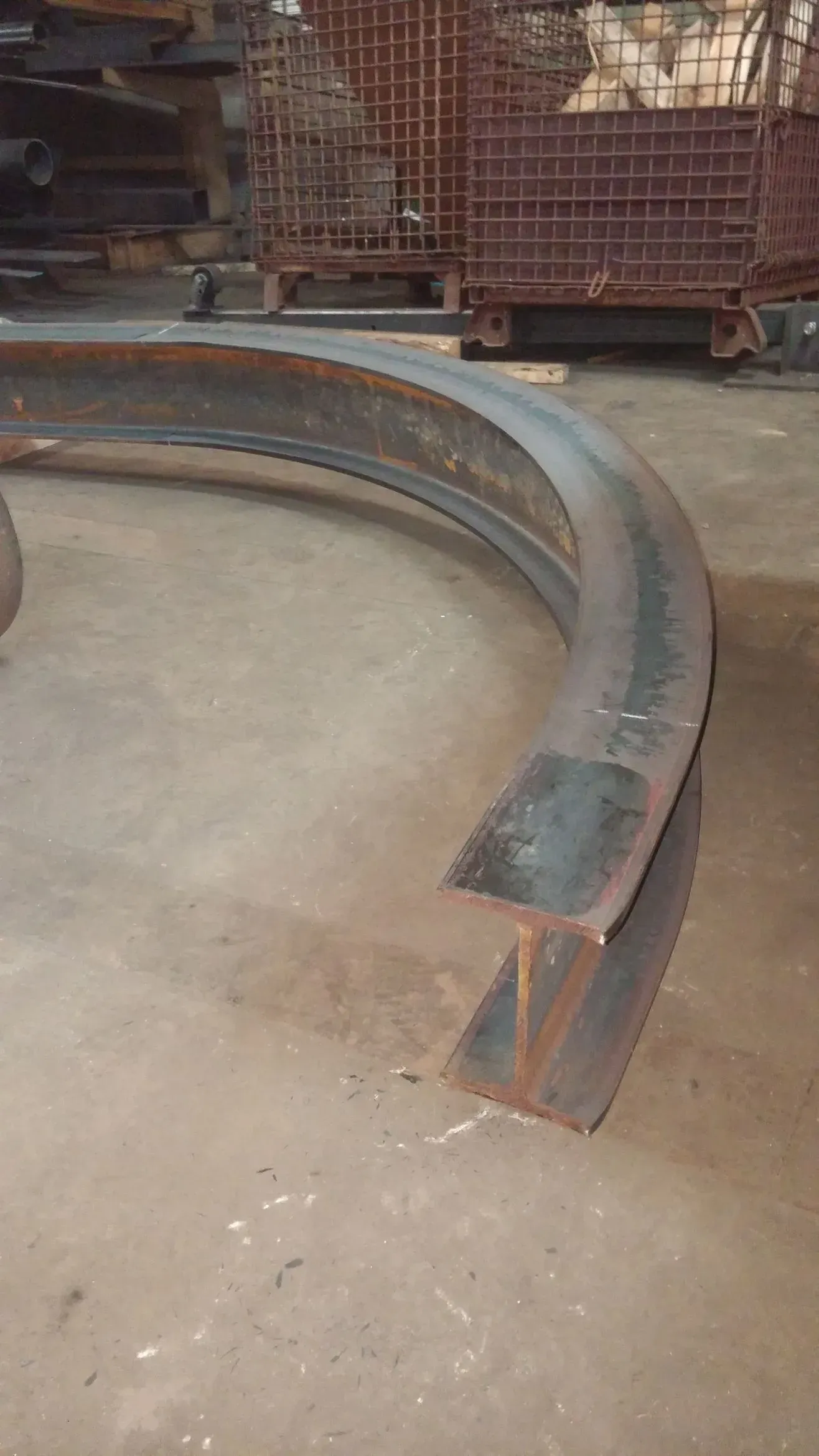 Curved steel beam section on a concrete floor in a workshop setting.