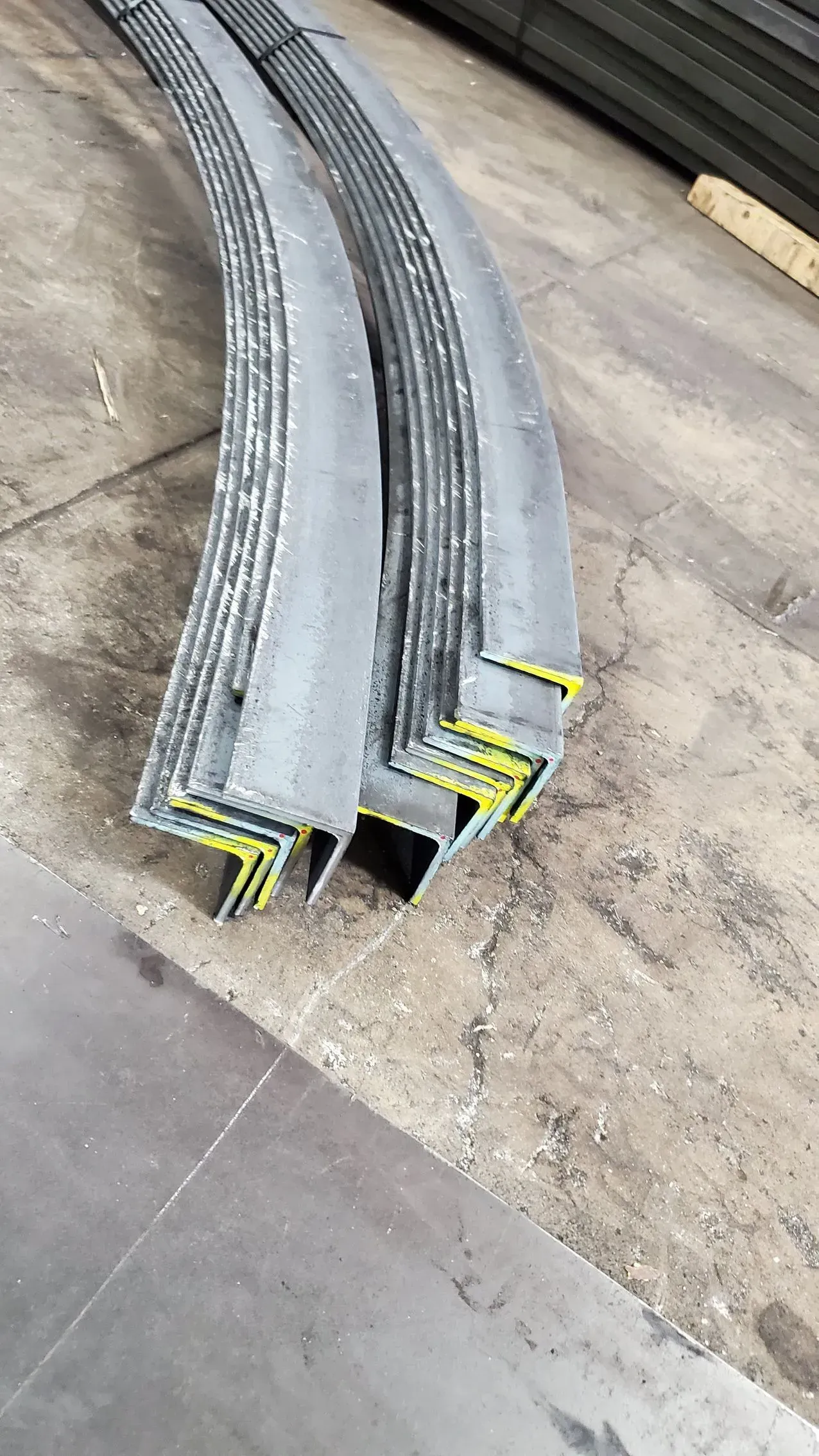 Curved metal L-beams stacked on a concrete surface, with yellow paint at their ends.