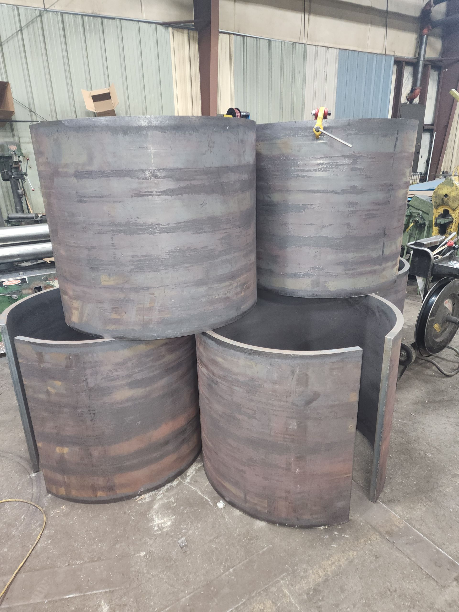 Four large, cylindrical metal pieces in a workshop; three intact, one open at the side.