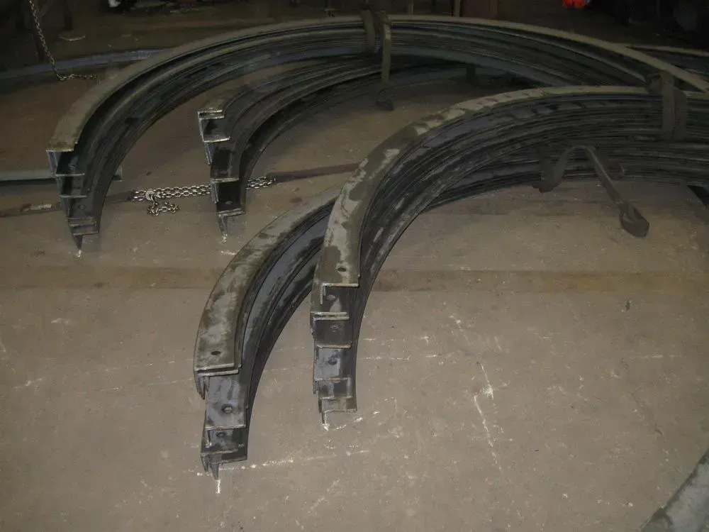 Curved steel beams with attached square supports, stacked on a metal surface.
