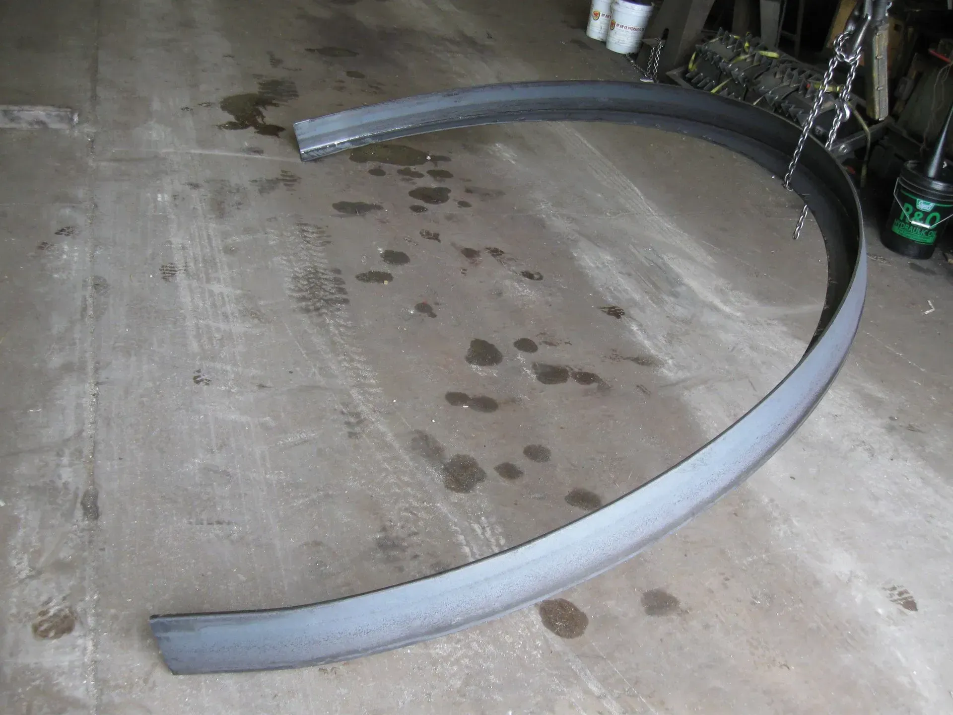 Curved, metal piece on a concrete floor with dark spots.