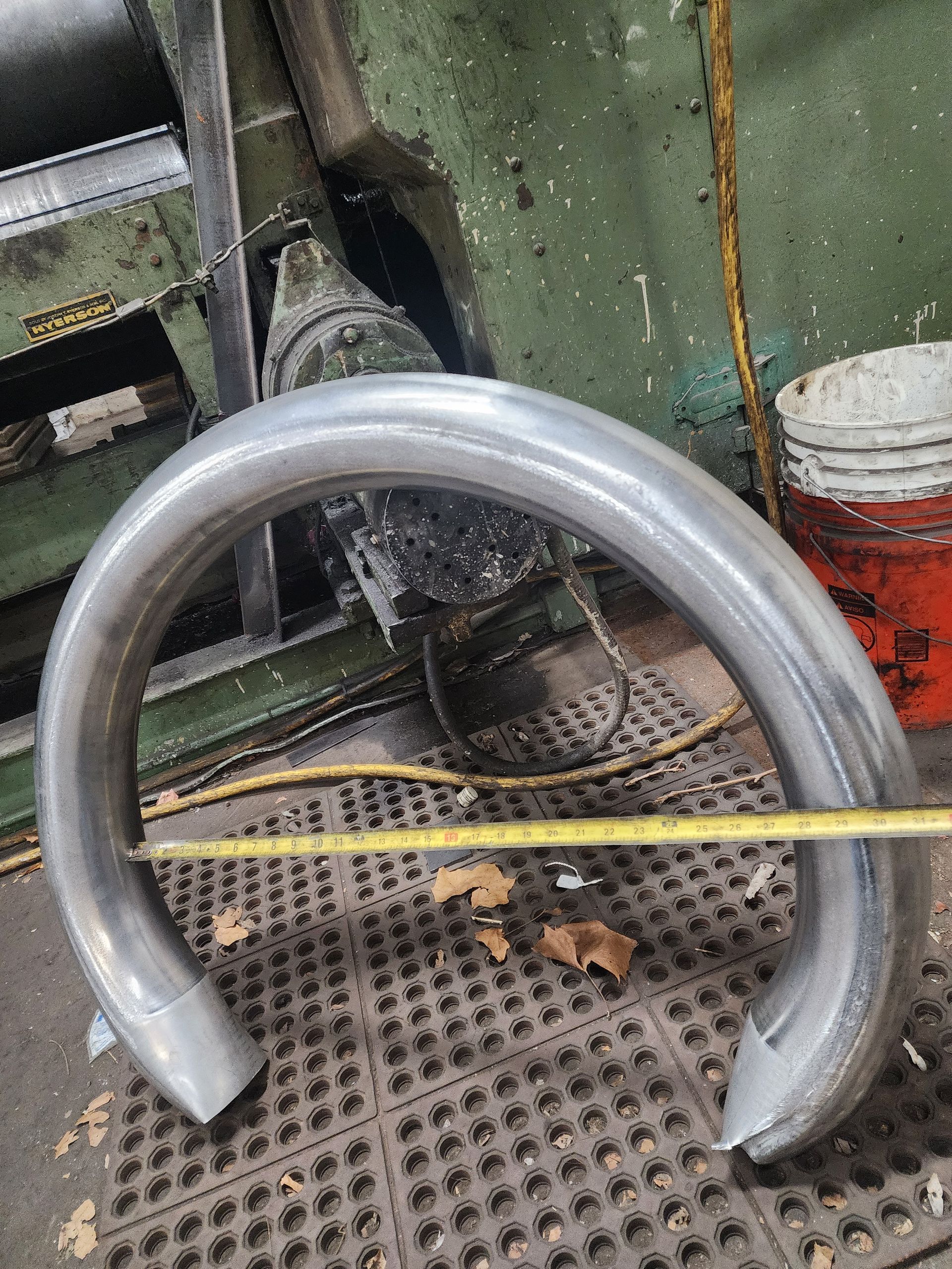 Bent metal tube on a shop floor with a tape measure.