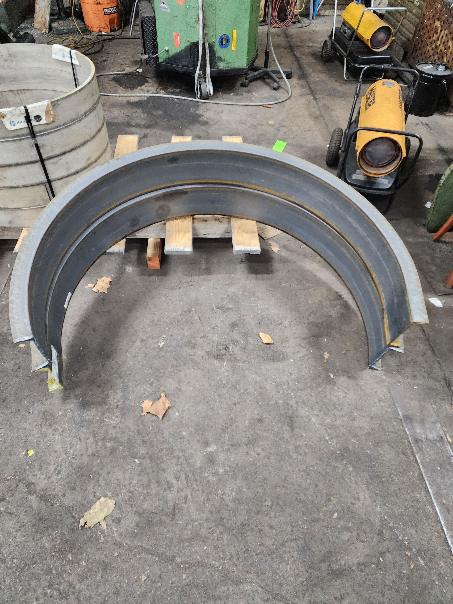 Arc-shaped metal component on a wooden pallet, in an industrial setting.